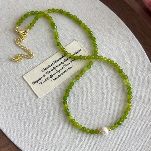 Detail of olive green faceted beads and white pearl on a gold-plated necklace