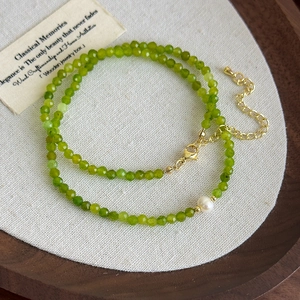 Macro detail of faceted green agate beads and a single white pearl on a gold clasp chain