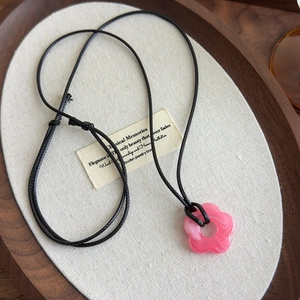 Détail du pendentif fleur rose en acrylique avec cordon noir sur un plateau en bois