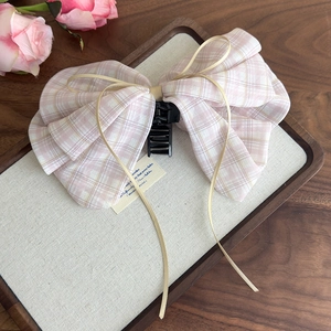 Detail of pink plaid bow hair claw clip with cream ribbon on a wooden tray with flowers