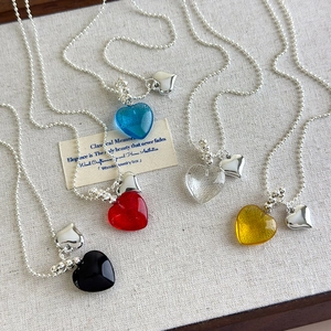 Macro shot of colorful glass heart pendants on silver bead chains against linen background