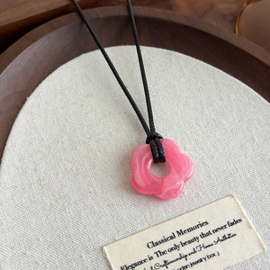 Détail du pendentif fleur rose en acrylique avec texture marbrée et cordon tressé noir