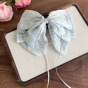 Detailed shot of a light blue plaid bow hair claw clip with long ribbons on a wooden tray