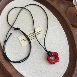 Détail du collier fleur en acrylique rouge avec texture marbrée et cordon noir réglable