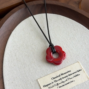 Détail d'un collier pendentif fleur rouge à cinq pétales sur un cordon noir tressé
