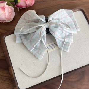 Detail of sweet plaid bow claw clip with cream ribbon tassels on beige tray