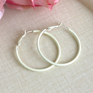 Close-up of cream matte metal hoop earrings on a textured background with floral accent