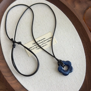 Gros plan détaillé du pendentif fleur bleue sur un collier en cordon noir tressé