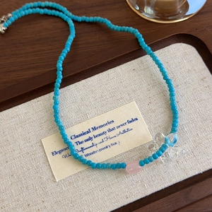 Collana di perline blu con ciondolo a fiore e perla rosa su un vassoio di legno