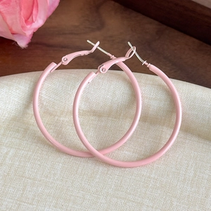 Close-up of pastel pink large hoop earrings with matte finish on elegant display tray