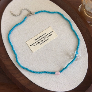 Dettaglio collana di perle blu con perla di calcedonio rosa e ciondolo farfalla