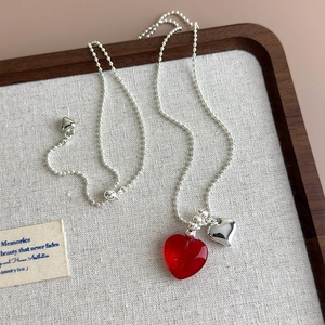 Detail of beaded necklace featuring a red translucent heart and polished silver pendant