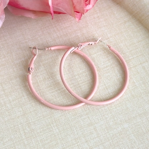 Detailed view of pink macaron hoop earrings with matte finish on textured fabric