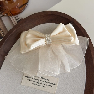 Close-up of cream satin bow hair clip with layered organza and triple-row pearl detail