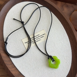 Détail du pendentif fleur en acrylique vert émeraude sur cordon noir et plateau en bois