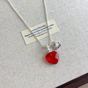 Detailed close-up of a red resin heart pendant and silver metallic charm on bead chain