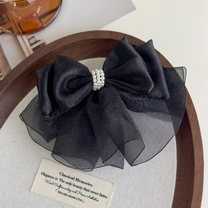 Macro detail of black satin and organza bow clip with triple-row pearl embellishment