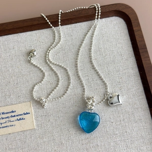 Detail of blue translucent heart pendant with silver bead chain and small metal charm