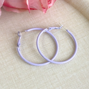 Detail showing lavender matte finish on large metal hoop earrings over textured fabric