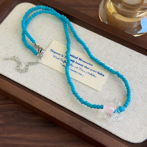 Dettaglio della collana di perline blu con pendente a farfalla rosa e chiusura in metallo