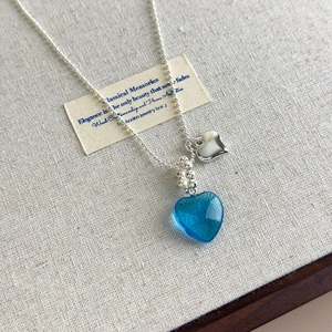 Detailed close-up of blue textured heart pendant and silver bead chain on linen background