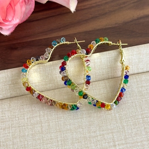 Détail de boucles d'oreilles cœur dorées avec perles en cristal coloré et fil enroulé
