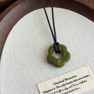 Détail du pendentif fleur en acrylique vert ajouré sur un cordon tressé noir