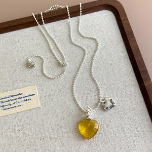 Detail of amber resin heart pendant and silver beaded chain on a rustic wooden tray