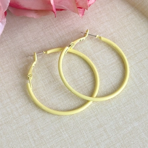 Detailed close-up of yellow macaron hoop earrings on an elegant beige fabric texture