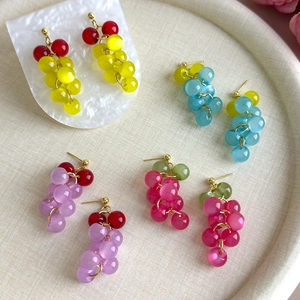 Detailed macro view of colorful grape-shaped beaded earrings on a white textured tray