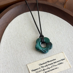 Détail d'un pendentif fleur en résine marbrée verte sur un collier en cordon noir