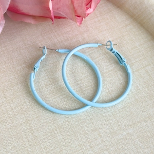 Close-up of blue macaron hoop earring on beige fabric with soft rose petals