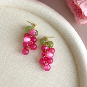 Detail of grape-shaped beaded earrings with pink and green stones on a woven texture
