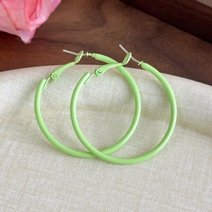 Close-up of bright lime green macaron-style hoop earrings on a textured beige background