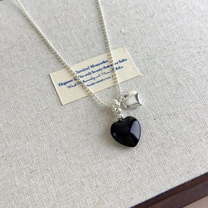 Detail of silver and black double heart pendants on a beaded chain necklace