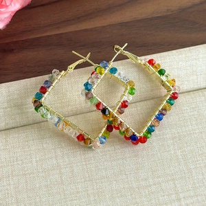 Détail de boucles d'oreilles carrées en fil doré avec perles de cristal colorées