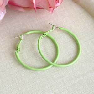 Detail of neon green large hoop earrings with matte finish on textured fabric