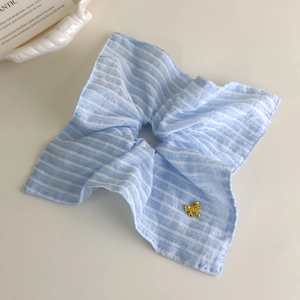 Détail d'un chouchou à rayures bleu clair avec un pendentif nœud doré sur plateau blanc
