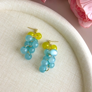 Detail of blue and yellow cat-eye beaded grape drop earrings on a beige textured tray
