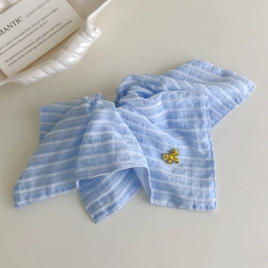 Détail d'un chouchou à rayures bleu clair avec une plaque nœud doré sur fond blanc