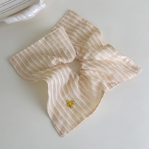 Gros plan d'un chouchou à rayures beige et blanc avec un petit pendentif nœud doré