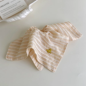 Détail d'un chouchou en tissu à rayures beige avec un accessoire de nœud doré