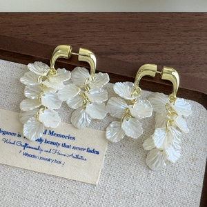 Detail von Muschelblüten-Ohrhängern mit Goldhaken auf rustikalem Vintage-Hintergrund