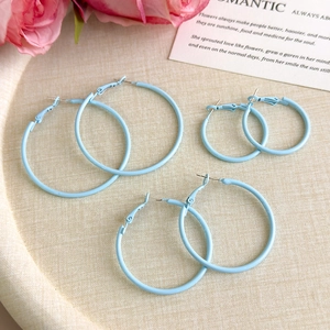 Three pairs of light blue hoop earrings in varying sizes on a textured beige tray