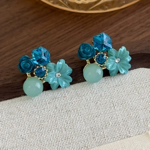 Detailed close-up of crystal flower stud earrings with blue resin rose and gold metal
