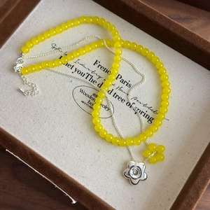 Détail du collier de perles jaunes avec pendentif fleur en argent sur velours brun