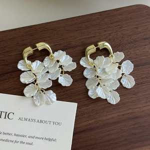 Elegante Ohrringe mit weißen Muschelblüten und goldenen Metallschlaufen auf Holz