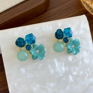 Macro detail of blue crystal flower earrings with resin roses and gold-tone base