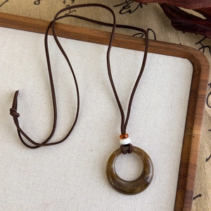 Gros plan du pendentif anneau en résine marron avec perle orange et cordon tressé fin