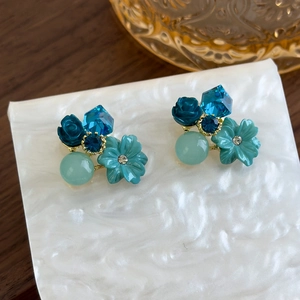 Detailed close-up of blue crystal flower earrings with teal resin rose on marble